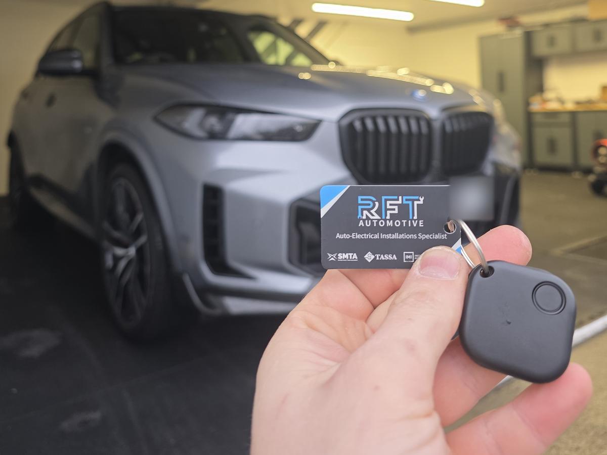 RFT Automotive tracker tag and card held up in front of a BMW X5 after installation